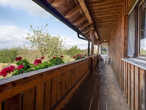 Eine Holzterrasse mit Geländer, Tisch und Stühlen, mit Blick auf einen Garten mit roten Blumen und Bäumen.