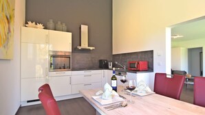 A modern kitchen with white cabinets, a built-in oven, a microwave, and a wine bottle on the counter. - Das Kuenstlerhaus in Kammerstein (Kammerstein)