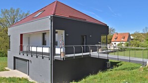 A modern two-story building with a red roof, a covered outdoor area, and a small bridge leading to a neighboring house. - Das Kuenstlerhaus in Kammerstein (Kammerstein)