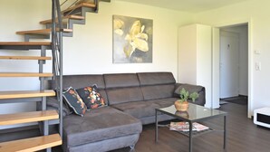 A modern living room with a grey sofa, a glass coffee table, and a wooden staircase. - Das Kuenstlerhaus in Kammerstein (Kammerstein)