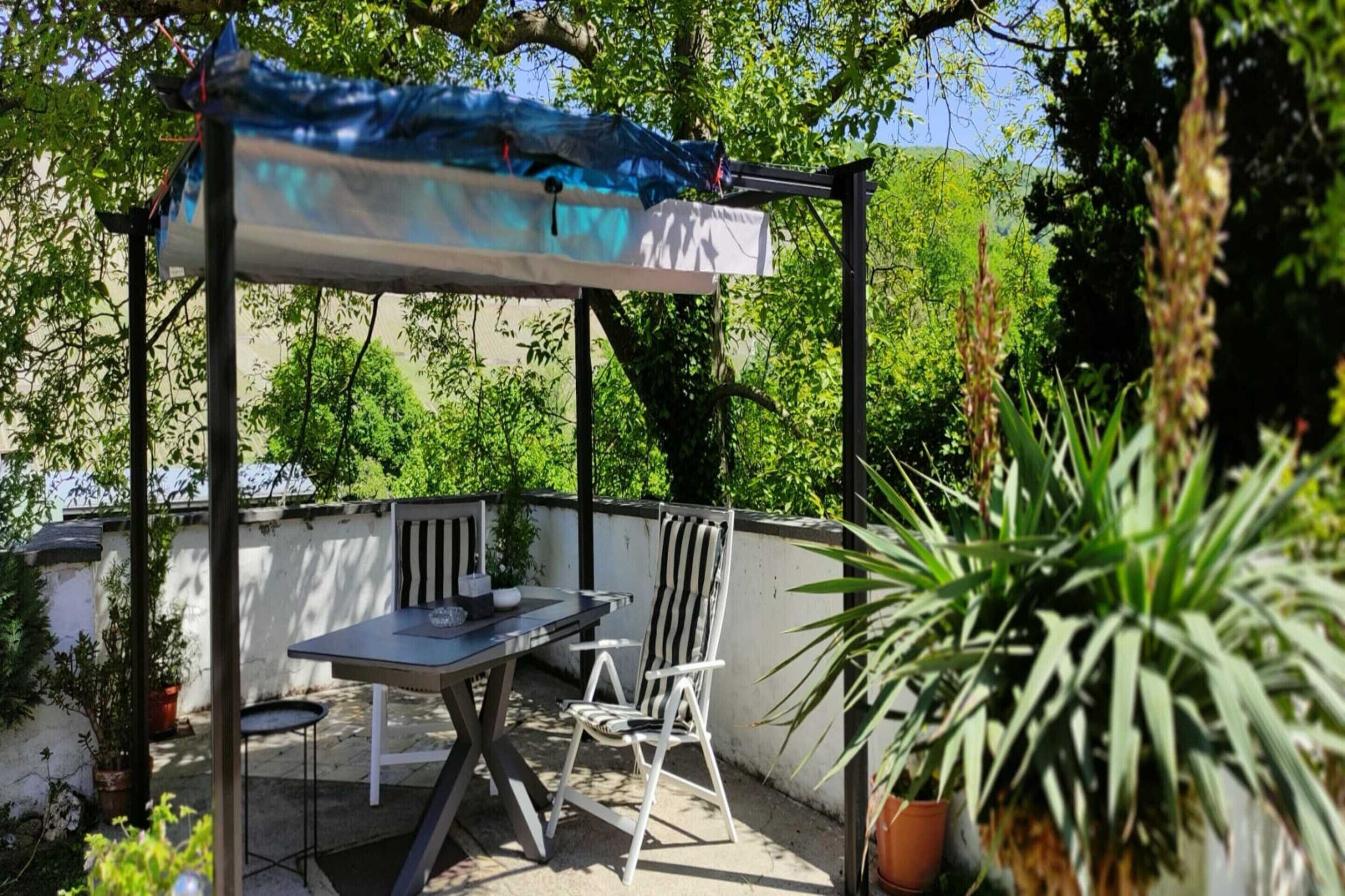 An outdoor patio with a table and chairs, a covered area, and potted plants.