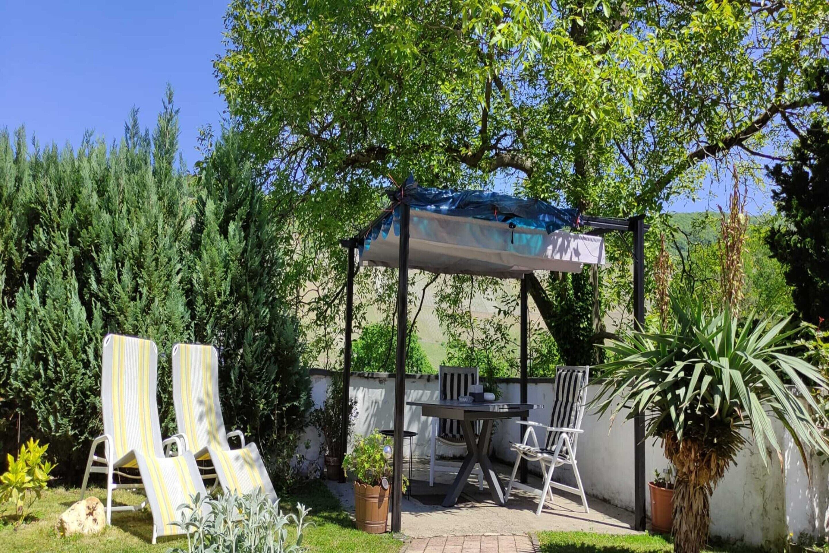 A covered patio area with a table and chairs, surrounded by greenery and a view of the countryside.