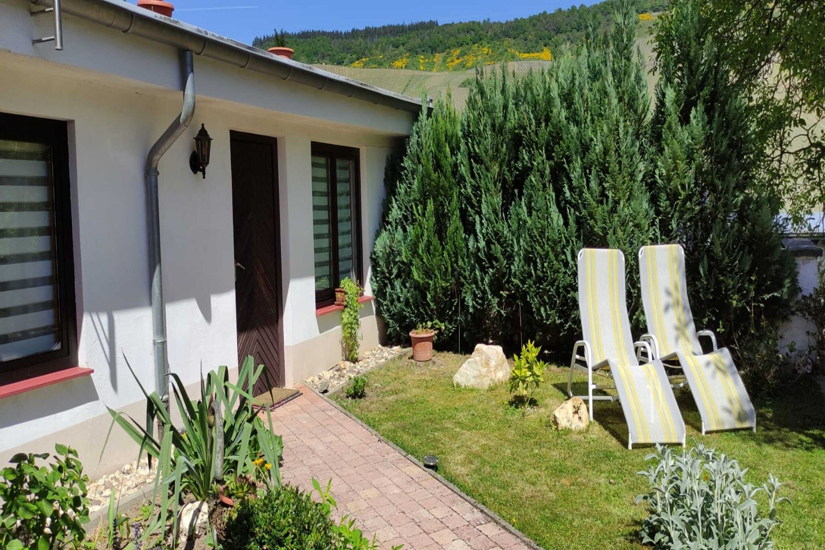 A house with a paved patio, two lounge chairs, and a garden with various plants.