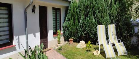 A house with a paved patio, two lounge chairs, and a garden with various plants.