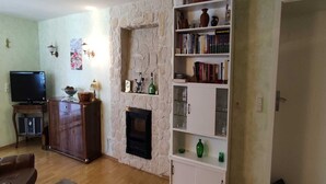 A living room with a stone fireplace, wooden cabinet, and a bookshelf filled with books and decorative items. - Apartment in Wehlen by Moselle Vineyards (Bernkastel-Kues)