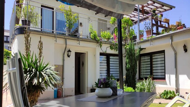 A patio with a table and chairs, surrounded by potted plants and a balcony with hanging plants. - Apartment in Wehlen by Moselle Vineyards (Bernkastel-Kues)