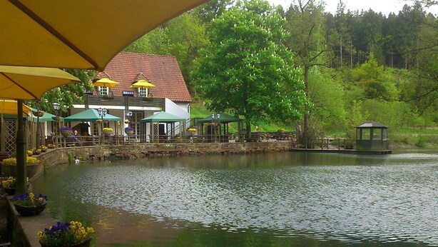 A lakeside restaurant with outdoor seating and umbrellas, a gazebo, and a small pavilion by the water. - Flat in Bellenberg With Sunbathing Lawn (Horn-Bad Meinberg)
