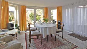 A dining area with a round table, chairs, and a view of the garden through large windows. - Flat in Bellenberg With Sunbathing Lawn (Horn-Bad Meinberg)