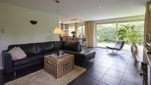A living room with a black leather sofa, a wicker coffee table, and a view of the outdoors through a large sliding glass door. - Holiday Home in Kortgene Near Lake Veere (Kortgene)