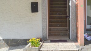 Una scala conduce all'ingresso di un edificio, con un piccolo vaso di fiori gialli e un muro in mattoni.