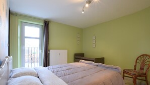 A bedroom with a bed, a chair, a radiator, and a window with curtains.