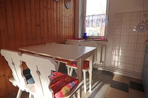 A wooden interior with a white table and chairs, a window with a view, and a tiled wall. - Cozy Bungalow in Stove Germany near Baltic Sea (Boiensdorf)