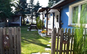 Une clôture en bois avec un portail, une cour gazonnée, un barbecue et une maison à l’extérieur bleu.