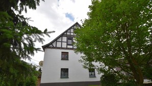 Ein traditionelles Fachwerkhäuschen mit symmetrischer Fassade, einem zentralen Eingang und einem gepflegten Rasen.