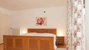 Ein Schlafzimmer mit einem Holzbett, einem Nachttisch mit Lampe, einem Heizkörper und einem blumigen Vorhang.