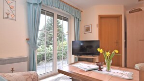 A living room with a television, a table with a vase of flowers, a sofa, and a door.