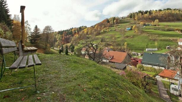 A rural landscape with a wooden bench, houses, and a hill with autumn foliage. - Quiet Home Near Vessertal (Schleusegrund)
