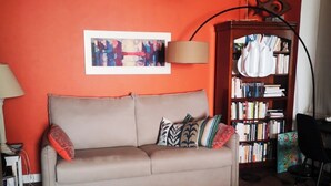 Ein Wohnzimmer mit einem beigen Sofa, einem blauen Teppich, einem Bücherregal und einer roten Wand.