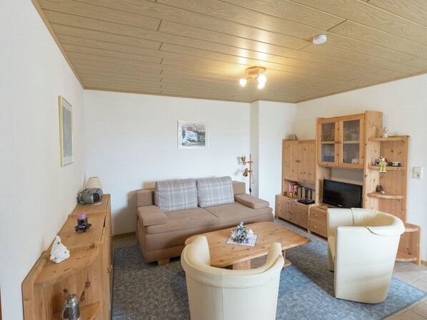 A cozy living room with a sofa, two armchairs, a wooden coffee table, and a TV. There is a wooden cabinet with glass doors and a small shelf with decorative items. - Wohnung in Bad Grund (Bad Grund)