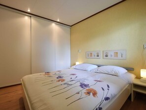 Un dormitorio con cama, mesita de noche, lámpara de pared y una puerta.