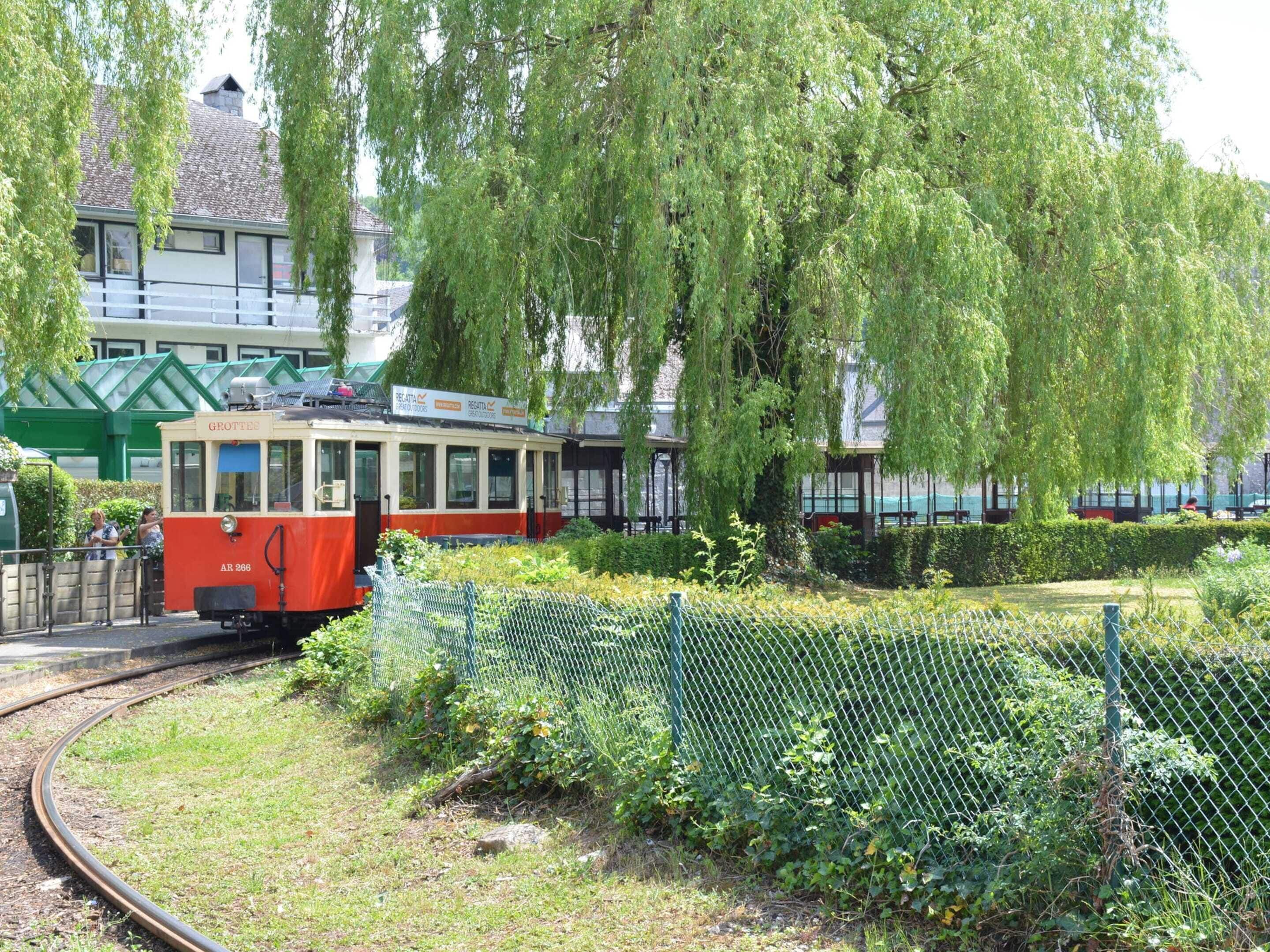 Un tramway rouge et blanc circule sur des rails, entouré de verdure et d’une clôture.