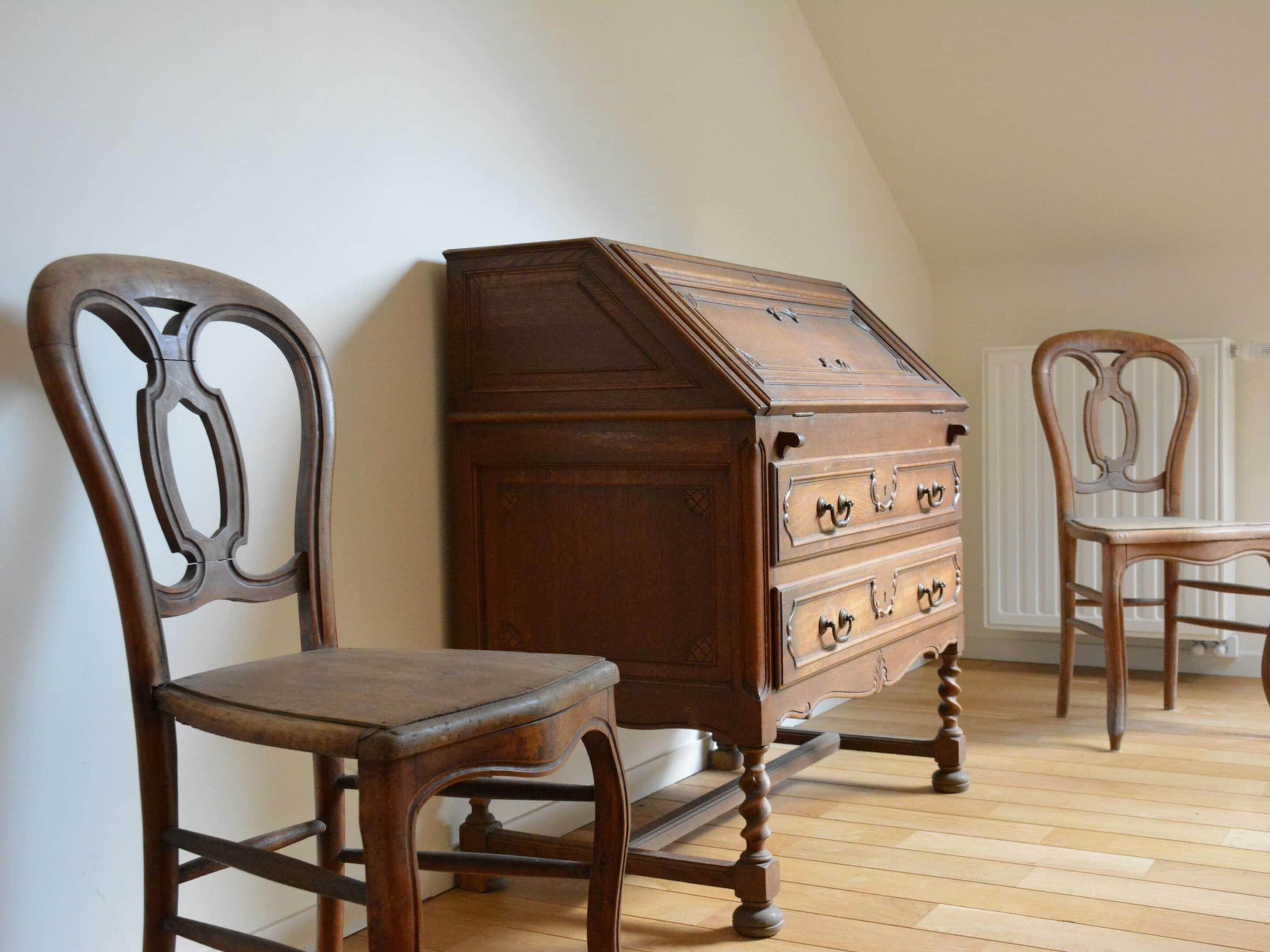 A room with two wooden chairs, a wooden dresser with drawers, and a white radiator.