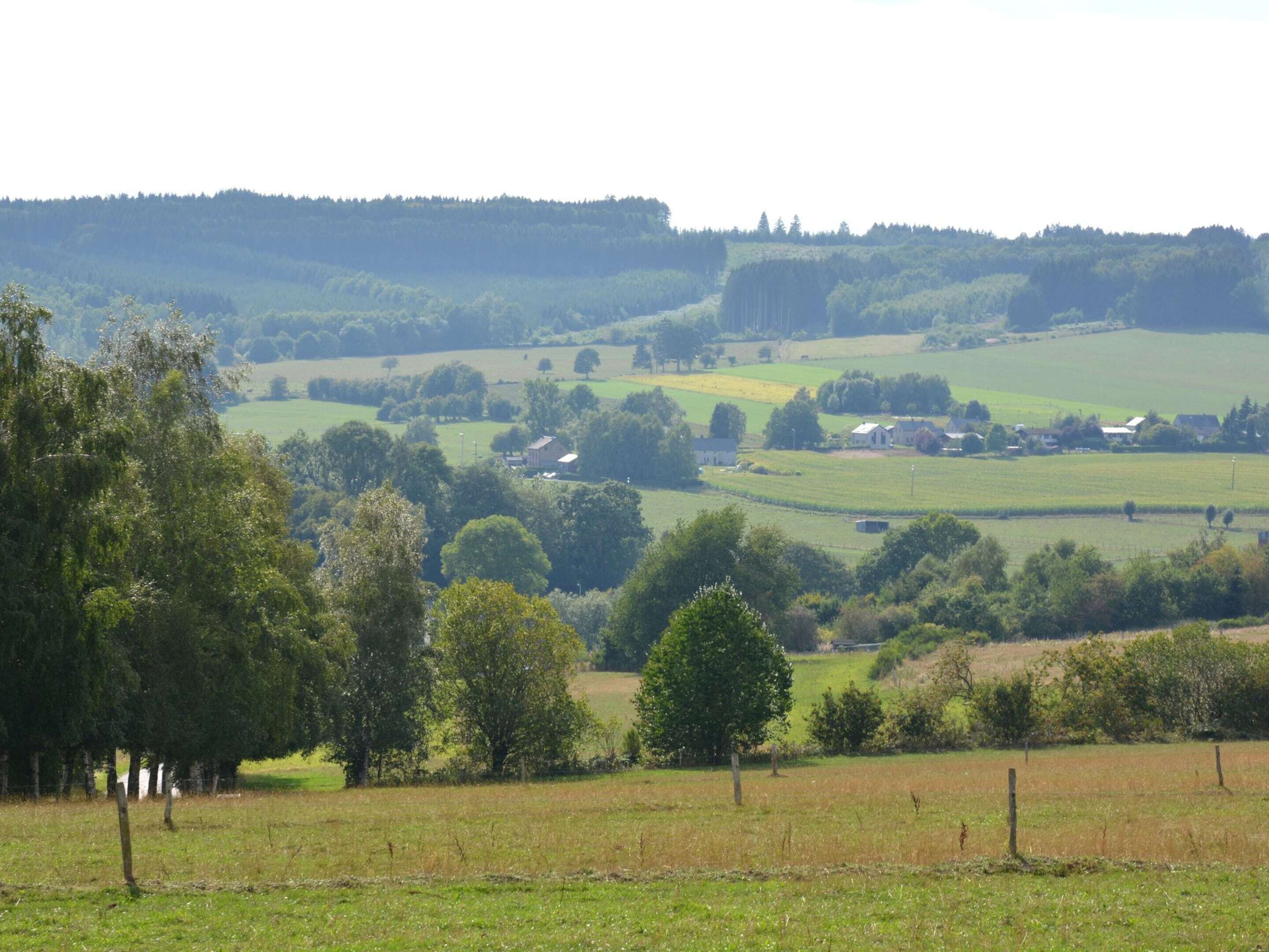 A rural landscape with rolling hills, scattered trees, and a few buildings in the distance.