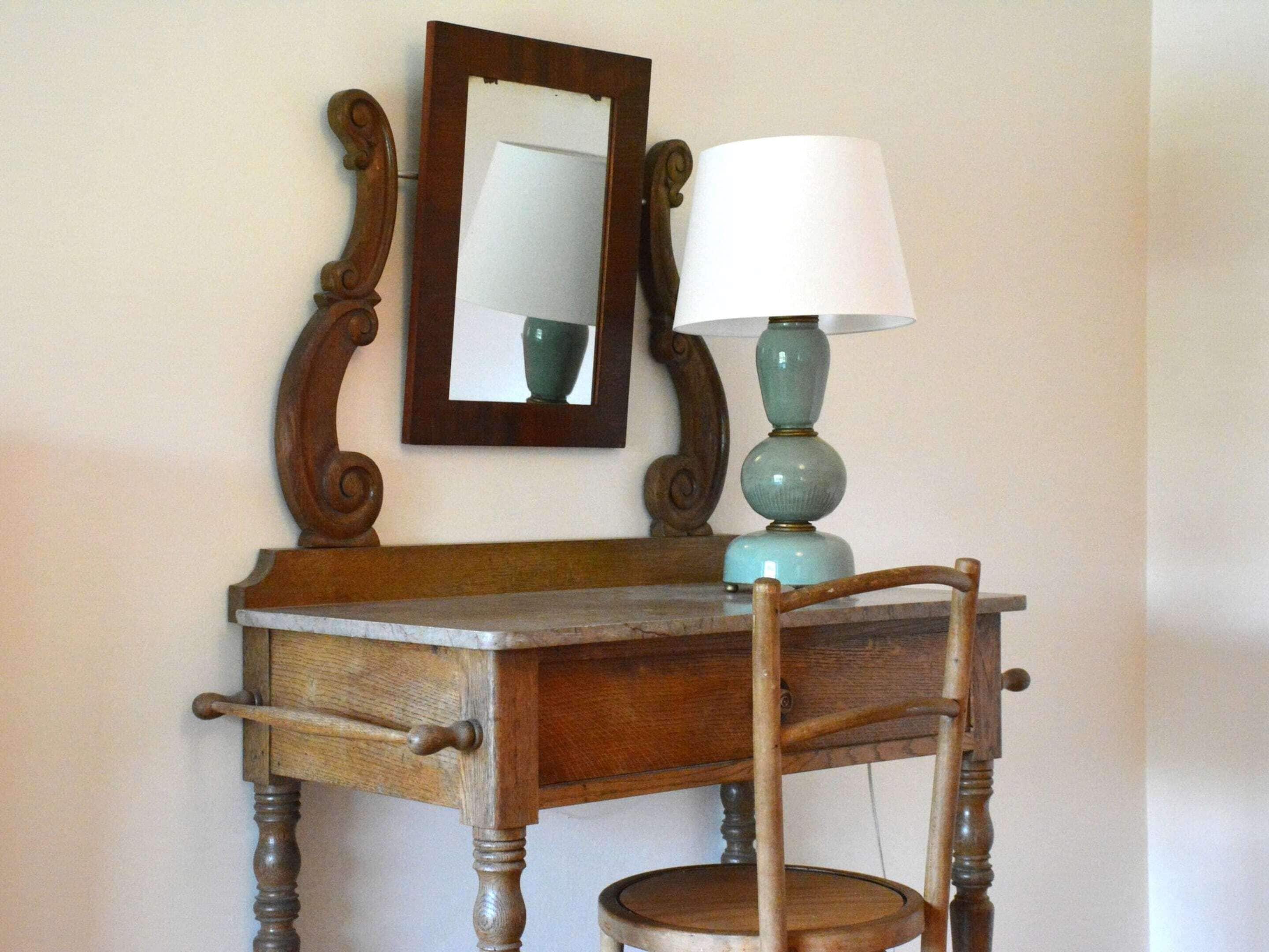 A wooden desk with a mirror and a lamp.