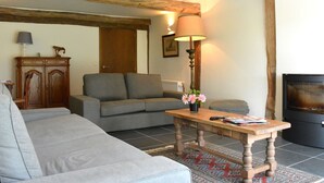Een woonkamer met een bank, een houten bijzettafeltje met een lamp, een open haard en een kast.