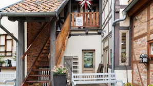 Un edificio tradicional europeo con una escalera de madera que conduce a un balcón, una banca blanca en el exterior y un letrero que indica un servicio de alquiler gratuito.
