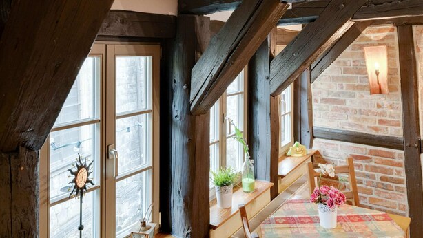 Una habitación rústica con vigas de madera a la vista, una pared de ladrillo y una escalera de madera.