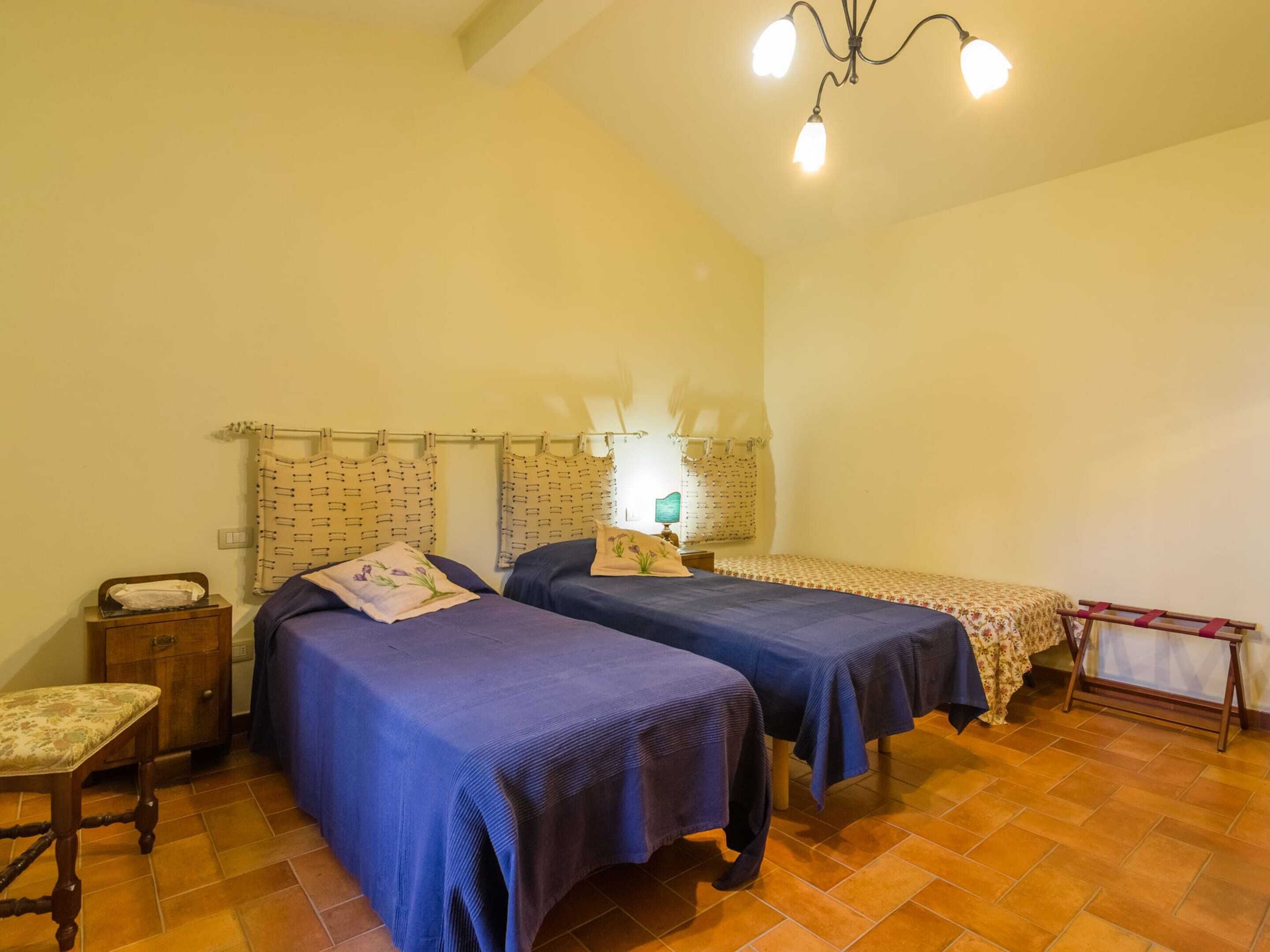 A bedroom with two beds, a wooden chair, a nightstand, and a hanging light fixture.