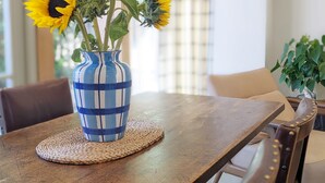A table with a blue and white striped vase containing sunflowers, a woven placemat, and a chair with a leather seat.