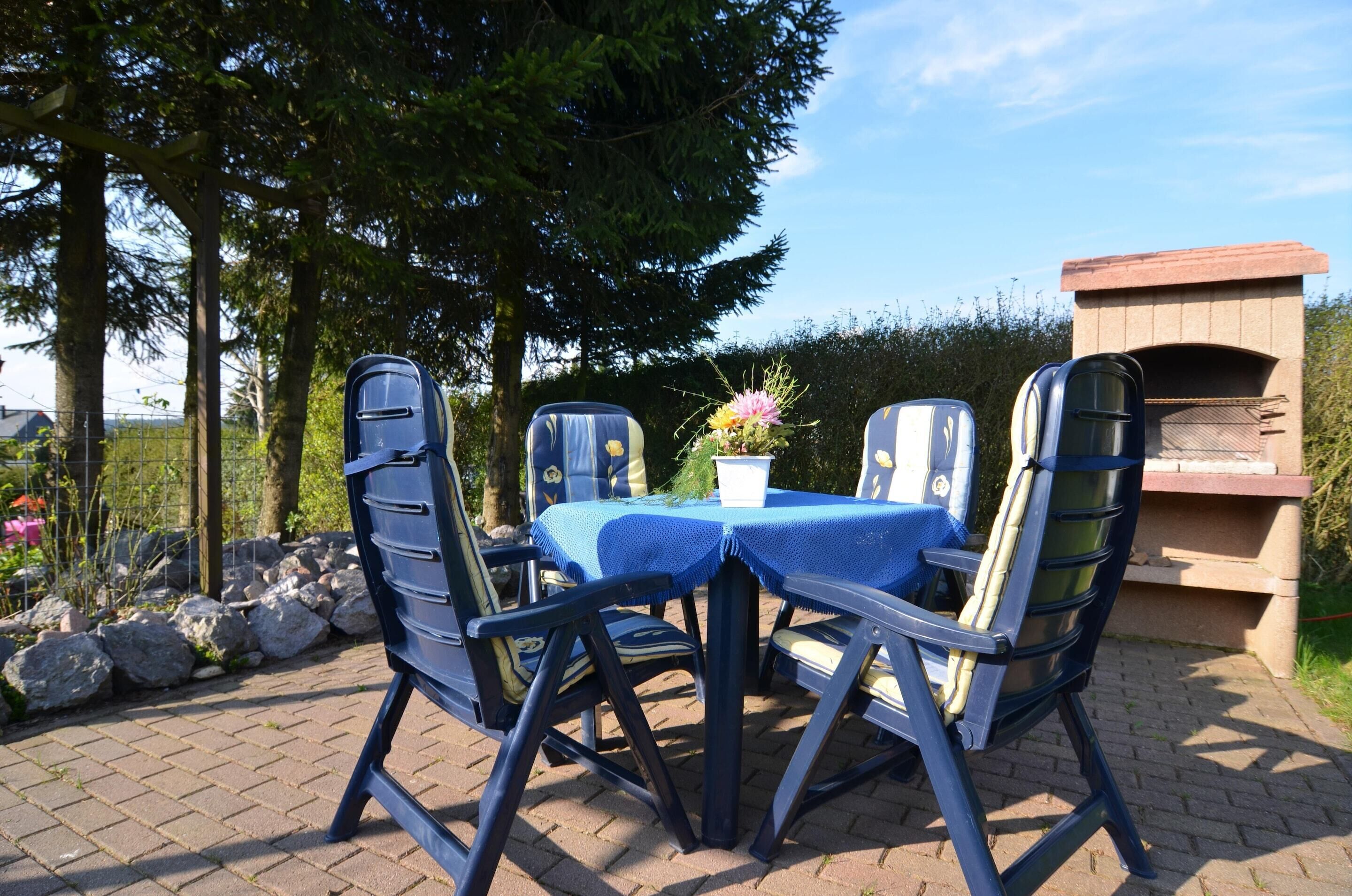 An outdoor patio with a table and chairs, a pizza oven, and a garden setting.