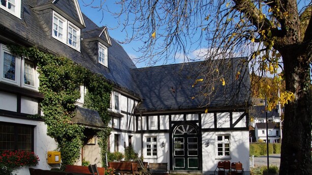 Um edifício tradicional em estilo de enxaimel com um pátio de calçamento, bancos e uma árvore com folhas de outono.