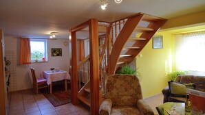 Uma sala de estar com escada de madeira, área de refeições e um sofá.