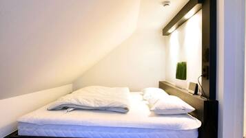 Cozy retreat with a single bed, nightstand, and shelf, perfect for a restful stay.