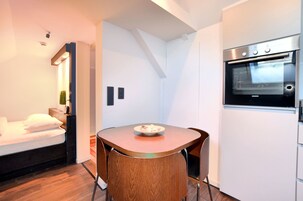 Una habitación compacta con cama, una mesa de comedor con sillas, horno empotrado y una pequeña cocina americana.