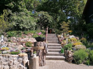 A stone staircase leading up to a wooden door, surrounded by a garden with various plants and flowers.