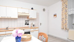 A modern kitchen with white cabinets, a sink, a stove, and a dining area with a table and chairs. - Spacious Apartment in Blankenburg Harz near Ski Area (Blankenburg)