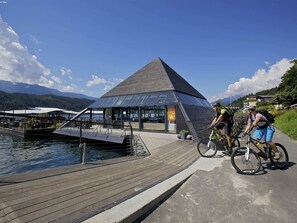 A pyramid-shaped building with a glass facade, a wooden deck, and a water body in the background. - Apartment in Fresach Near Lake Millstatt (Fresach)