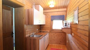 Pieni, kompakti puinen mökki, jossa on pieni keittiönurkkaus, yksi ikkuna ja punainen matto.