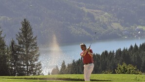 Golfaaja viheriöllä, taustalla järvi ja puita.