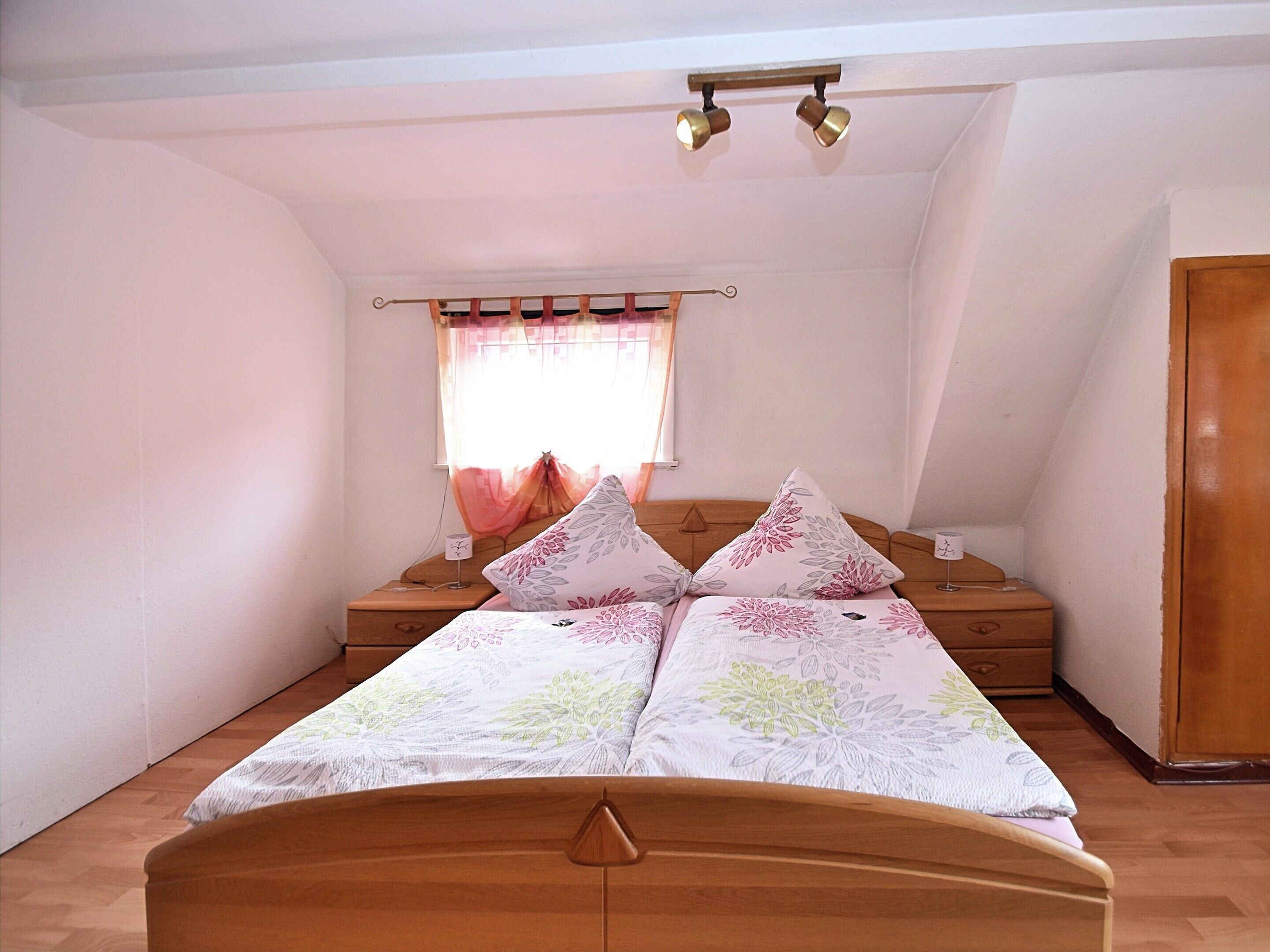 A bedroom with a wooden bed, a nightstand, a window with curtains, and a ceiling light fixture.