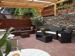 An outdoor patio area with a stone wall, wooden pergola, wicker furniture, and a potted plant. - Lavish Apartment in Merschbach near Forest (Merschbach)
