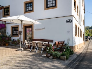 A building with a number '23' on the facade, a bench, a table with chairs, and an umbrella. - Lavish Apartment in Merschbach near Forest (Merschbach)