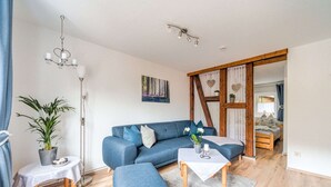 Una sala de estar moderna con un sofá azul, una mesita, una planta en maceta y piso de madera.