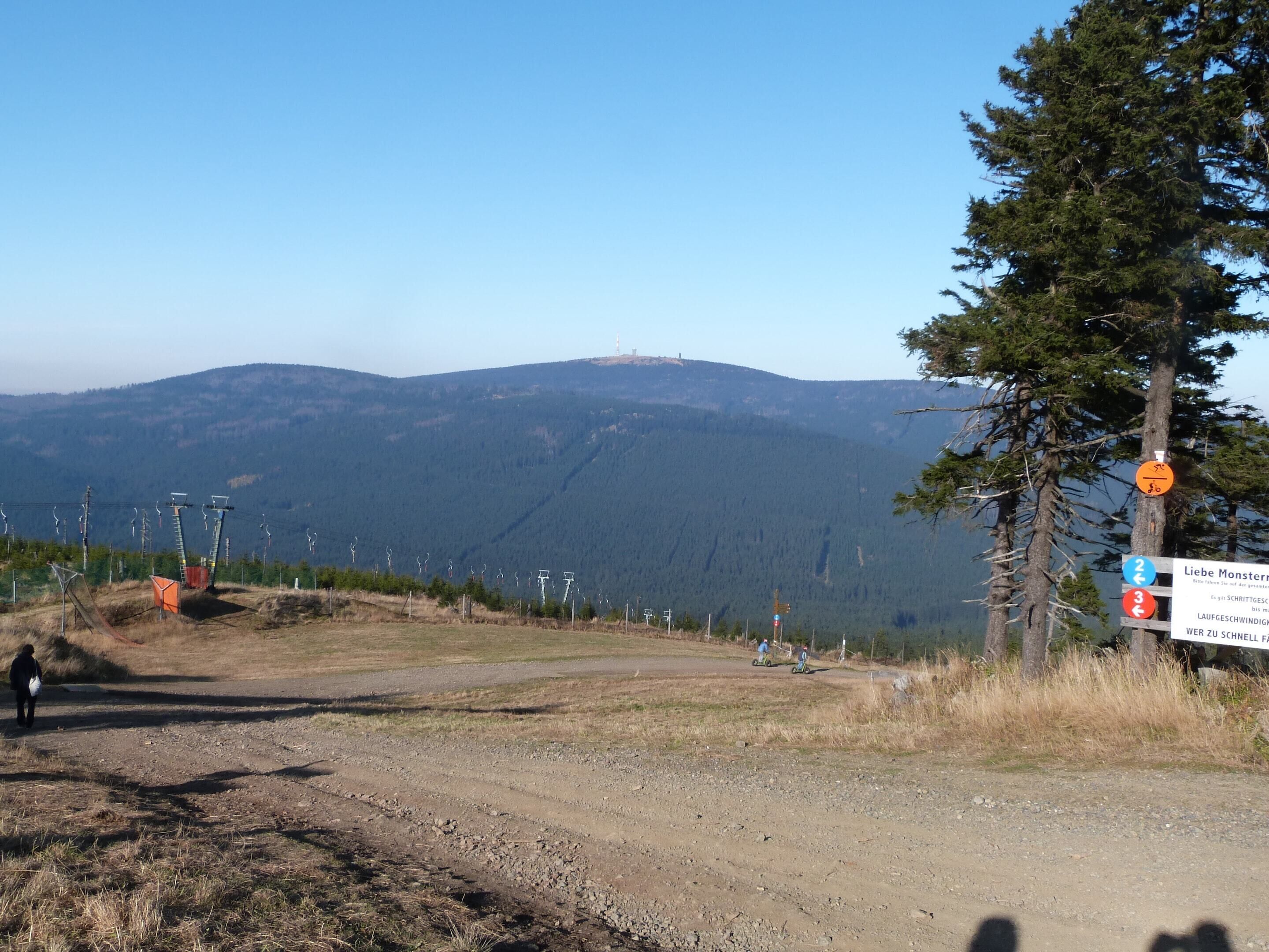 A mountainous landscape with a dirt path leading to a signpost indicating a hiking trail.
