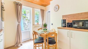 Una cocina acogedora con armarios de madera, una mesa de comedor con sillas, un reloj en la pared y una ventana con cortinas.