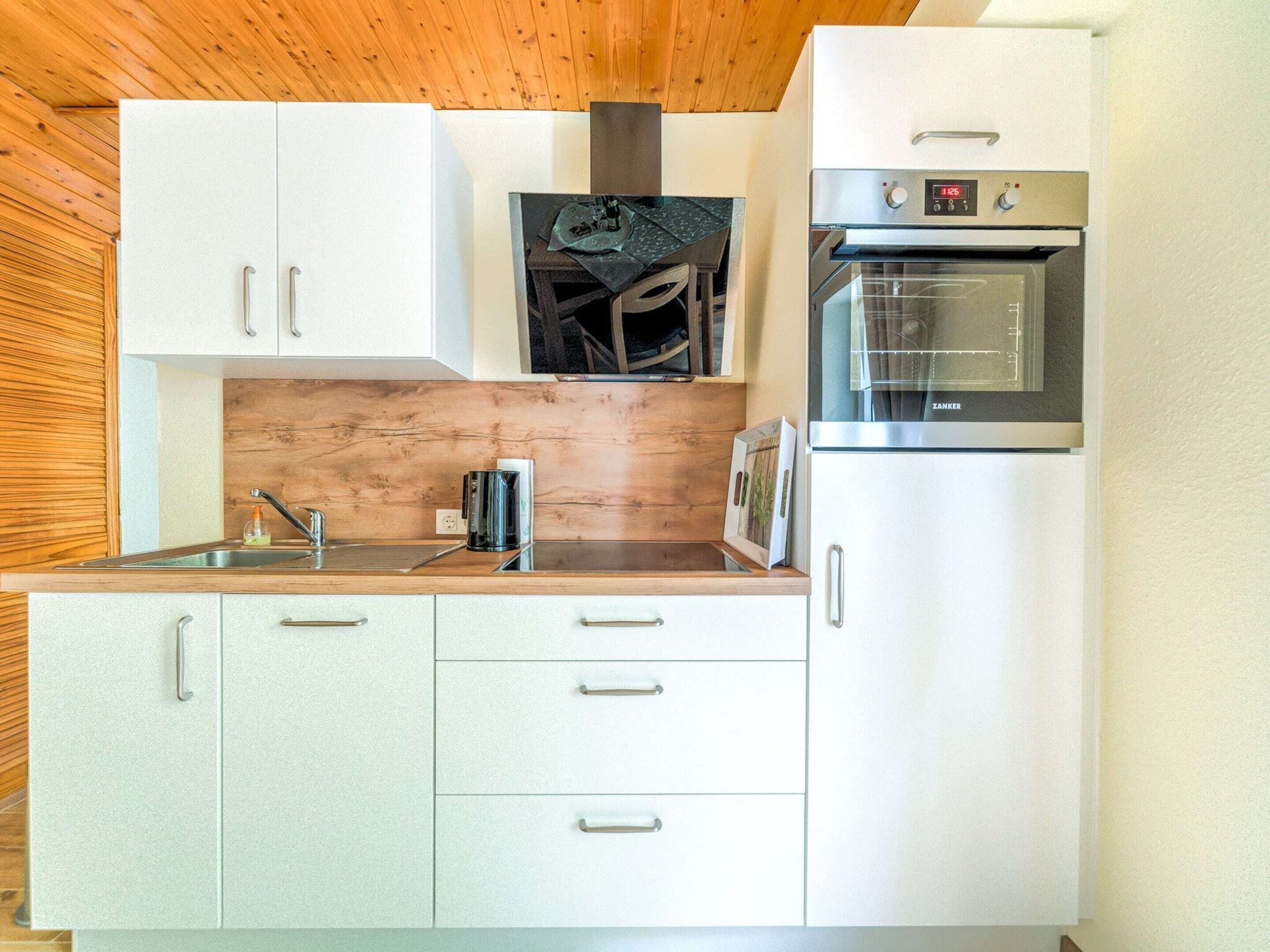 A compact kitchen with white cabinets, a stainless steel oven, and a wooden ceiling.